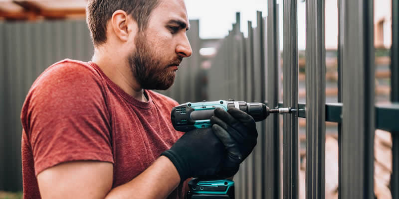worker installing a panel of an aluminum fence with a power drill
