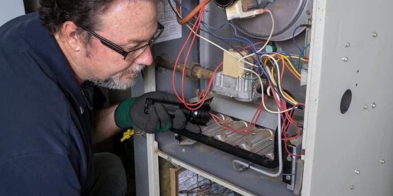 Technician looking over a gas furnace with a flashlight