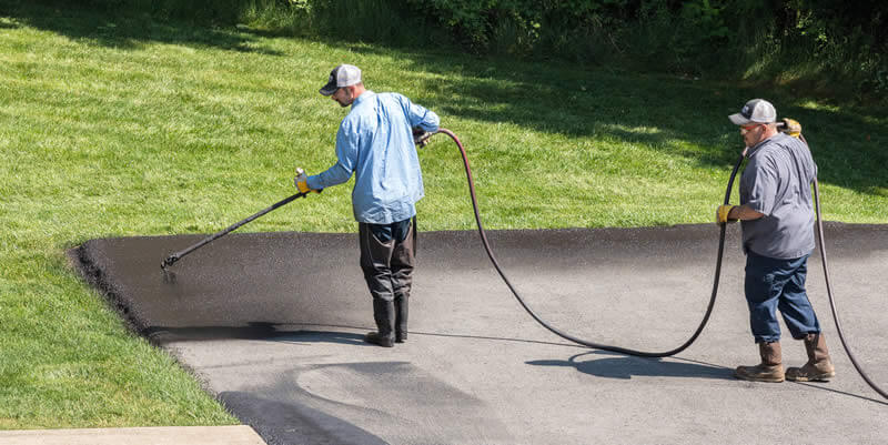 driveway pros applying driveway sealant with sprayer