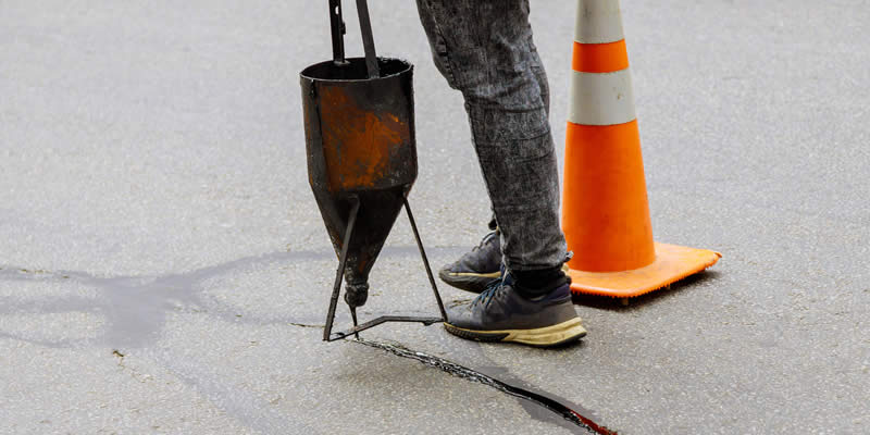 worker sealing cracks in asphalt driveway