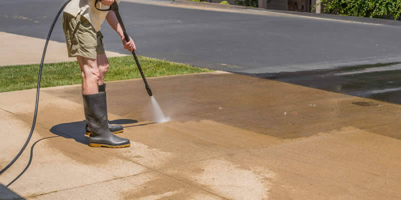 man pressure washing driveway with wand sprayer