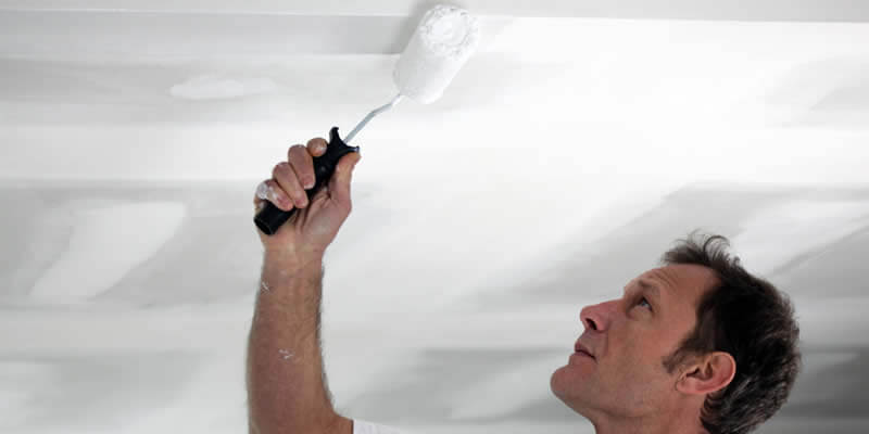 painter using roller to paint a ceiling