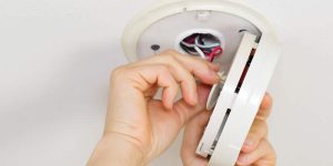 worker installing a wired smoke detector unit
