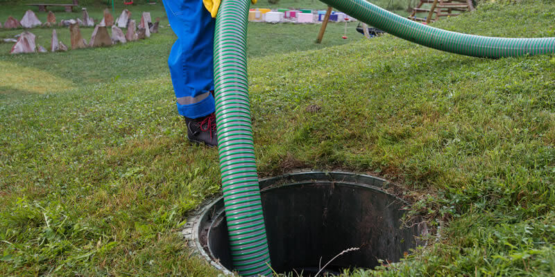 worker pumping out septic tank in backyard